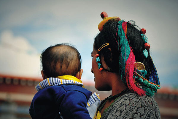 A Tibetan woman wearing traditional head decorations carries his baby. [Photo provided to China Tibet Online]