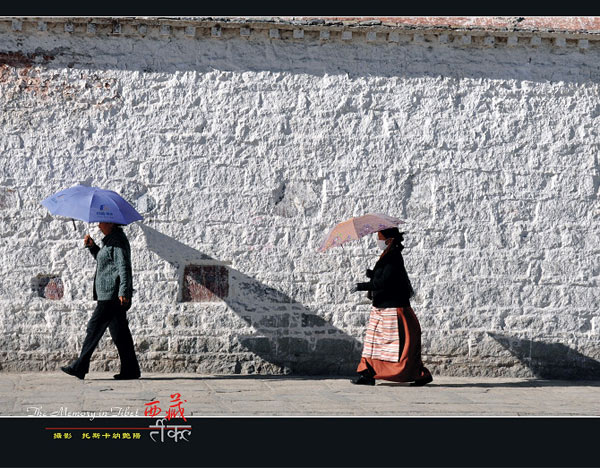Visitors carrying with umbrellas walk at the foot of the Jokhang Temple in Lhasa. [Photo/sina.com.cn]
