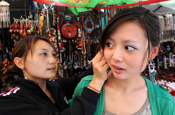 A girl (R) tries a pair of earrings in a shop on Barkhor Street in Lhasa, capital of southwest China's Tibet Autonomous Region, July 24, 2011. A large number of tourists poured into Tibet during the summer season, as the region is celebrating the 60th anniversary of its peaceful liberation. The region received 2.25 million tourists in the first half of this year, 24.8 percent more than the same period of last year. [Photo/Xinhua]