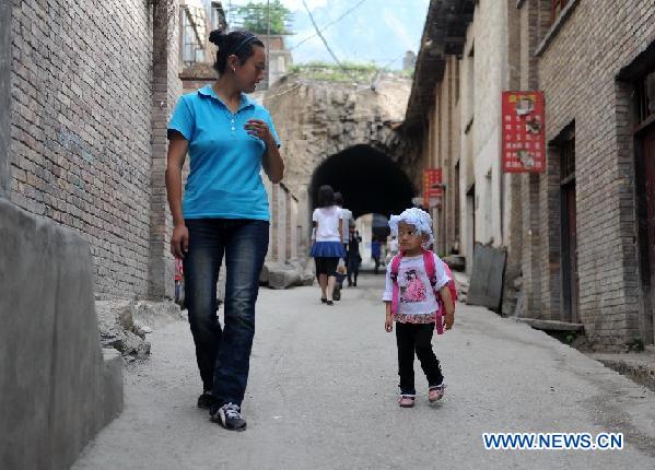 Wang Fangfang, a Tibetan woman, takes her 22-month-old daughter Nanka Wangmo to walk on the street at Zhouqu County, northwest China's Gansu Province, Aug. 3, 2011. On Aug. 8, 2010, the day Wang will never forget, the young Tibetan mother lost her house and her beloved husband who was on duty in a police office when a mudslide swept the county instantly. Wang now works in the Home For the Aged of Zhouqu, and takes Nanka with her anywhere she goes. Seeing workers busy in building new houses under cranes, Wang said she was filled with hope for the future. [Photo/Xinhua]