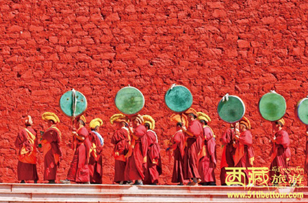 A "guard of honor" made up by lamas dressed in red capes presents a splendid view at the Buddha Painting Displaying Ceremony of the Ganden Monastery,  Lhasa, capital city of Tibet, looking grand and bright-bolored against the vivid red wall. [Photo/51tibettour.com]