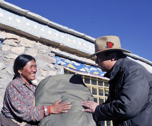 In this picture taken on December 5, 2011, Gao Baoping (R), a local government official sends winter relief materials to a farmer in Mami Village, Gaize County in Tibet Autonomous Region. A magnitude 4.9 earthquake hit the region on December 1. [photo/Xinhua]
