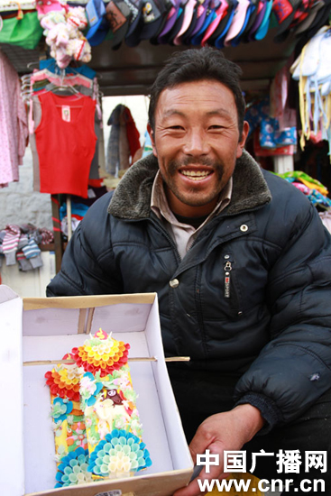 Butter sculpturer Kelzang poses for a picture with his product at a market in Lhasa, capital of southwest China's Tibet, before the Tibetan New Year. [Photo/CNR]