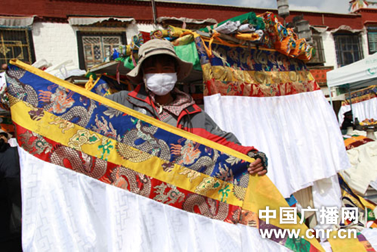  A Tibetan vendor measures the colorful colth, a Tibetan-style ornament hung above windows and doors, with creative design of dragon.[Photo/CNR]