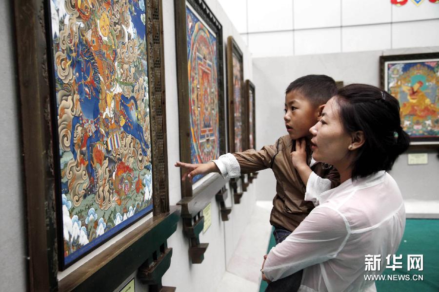 A local resident with her son was watching the Thangka painting displayed in a Manniang Thangka exhibition held in Lhasa, capital of southwest China's Tibet Autonomous Region, July 21. [Photo/Xinhua]