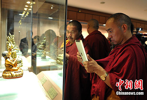 A monk took photos for the exhibits at an exhibition of returned Tibetan cultural relics at the regional museum of southwest China's Tibet, July 25. [Photo/Chinanews.com]