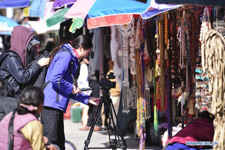 A tourist films vendors with a camera on a commerical street in Lhasa, capital of southwest China's Tibet Autonomous Region, April 3, 2013. Lhasa received 436,900 trips during the first quarter of thi