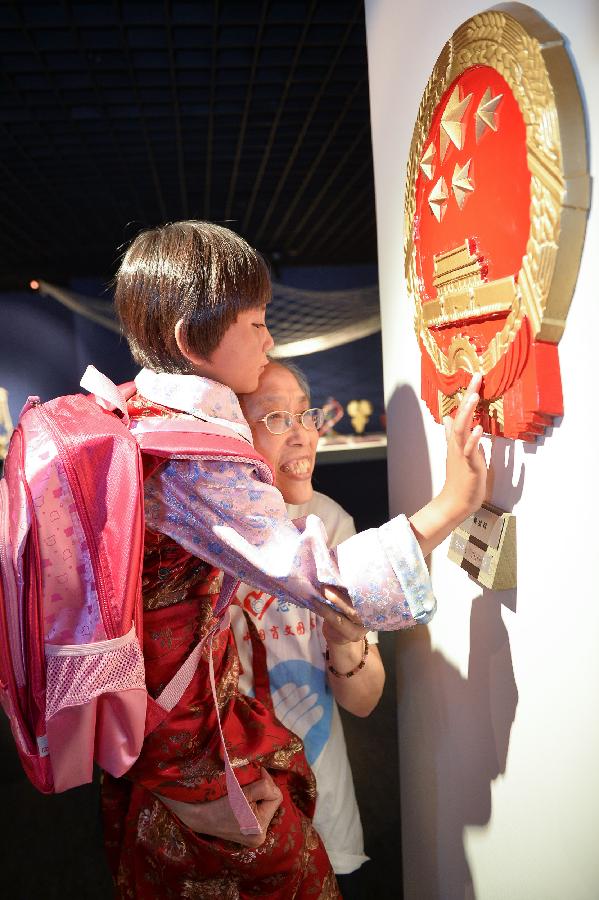 Nine-year-old girl from southwest China's Tibet Autonomous Region touches a model of national emblem with the help of a 67-year-old volunteer in the China Braille Library in Beijing, capital of China,