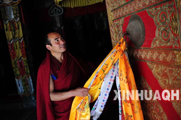 Photo shows a monk clears up the khadas tied on the gate of the scripture hall of the Lamo Dechen Monastery. [Photo/Xinhua]