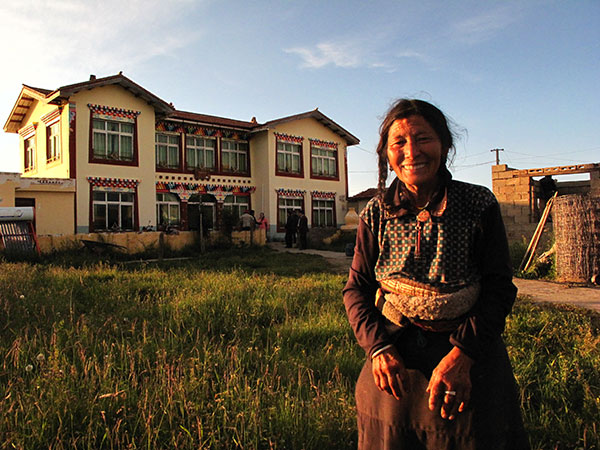 A Tibetan woman stands in front of a two-storied resettlement house in Banyou village, Ruo'ergai County, in the Aba Tibetan and Qiang Autonomous Prefecture. [Photo by Li Yang/China Daily]